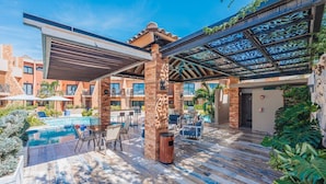 A poolside area with a covered seating area, a pool, and a building with a brick facade.