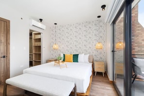 A modern bedroom with a large bed, bedside tables, a bench, and a sliding glass door to a balcony.
