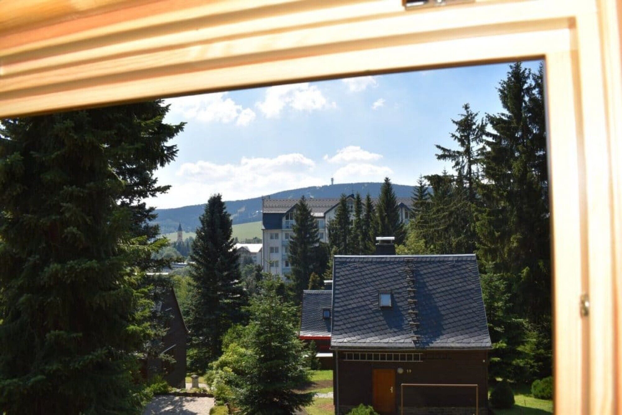 A view through a window of a residential area with houses, trees, and a distant hill.