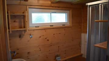 A wooden cabin bathroom with a window, a toilet, a sink, and a shower enclosure.