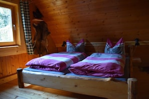 Une pièce de cabane en bois comprenant un lit, une fenêtre et un rideau à carreaux.