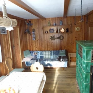 Une pièce chaleureuse avec un mur en bois, un canapé recouvert d’un tissu à motifs, un luminaire suspendu et un appareil électroménager vert.