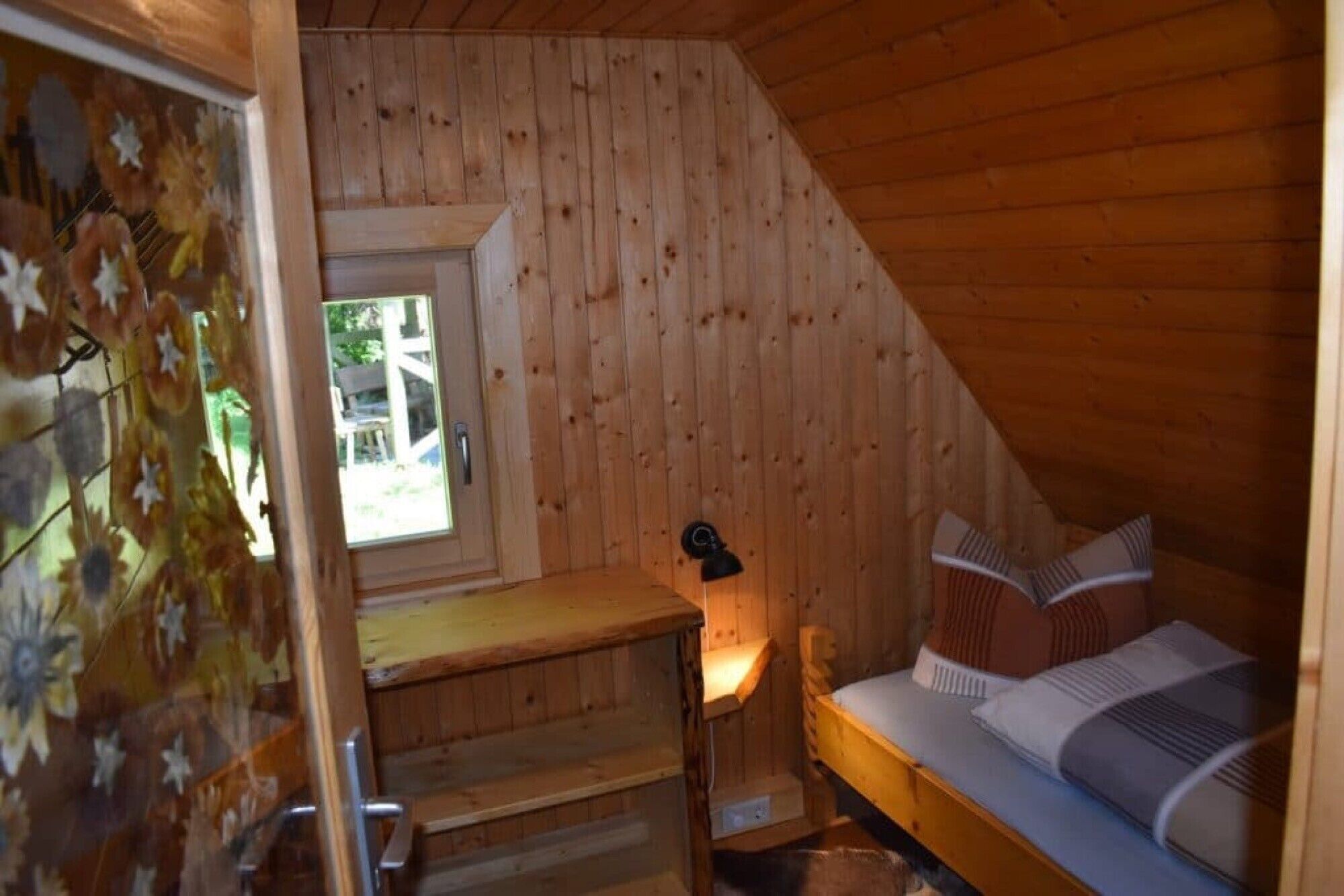 A wooden cabin room with a bed, a window, and a staircase.