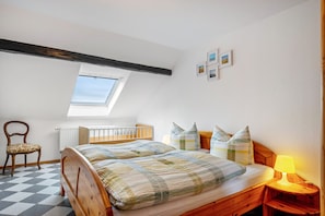 Une chambre à coucher avec un lit en bois, une petite table de chevet avec une lampe, une chaise, une fenêtre et un radiateur.