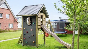 Een speelconstructie met een glijbaan en klimmuur in een gazon.