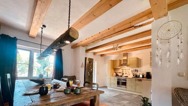 A rustic kitchen with wooden beams, a dining area with a wooden table, and a dreamcatcher on the wall. - Holiday Home 'Am Rande Des Spreewald' with Private Terrace, Private Garden and Wi-Fi (Heinersbrück)