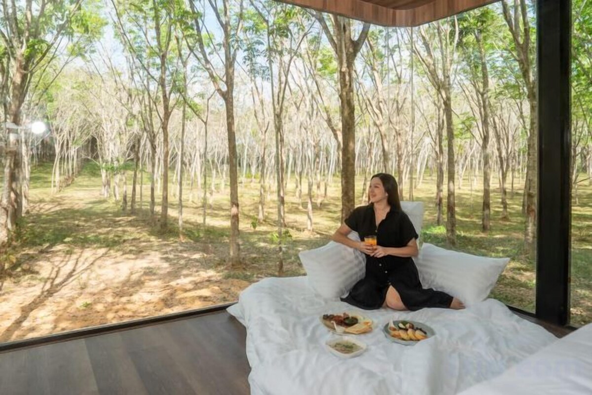 Una persona sentada en una cama con vista a un bosque.