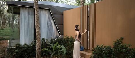 A modern, minimalist building with a large wooden panel wall, surrounded by trees and greenery.
