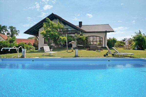 Una piscina con sillas de descanso, una casa con techo de tejas y un jardín con césped.