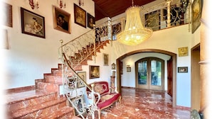 Un magnifique escalier orné de balustrades travaillées, un lustre et des œuvres d’art encadrées qui décorent les murs.