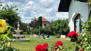 Un jardin agrémenté d’une fontaine, d’une statue et d’un bâtiment dont le toit est rouge.