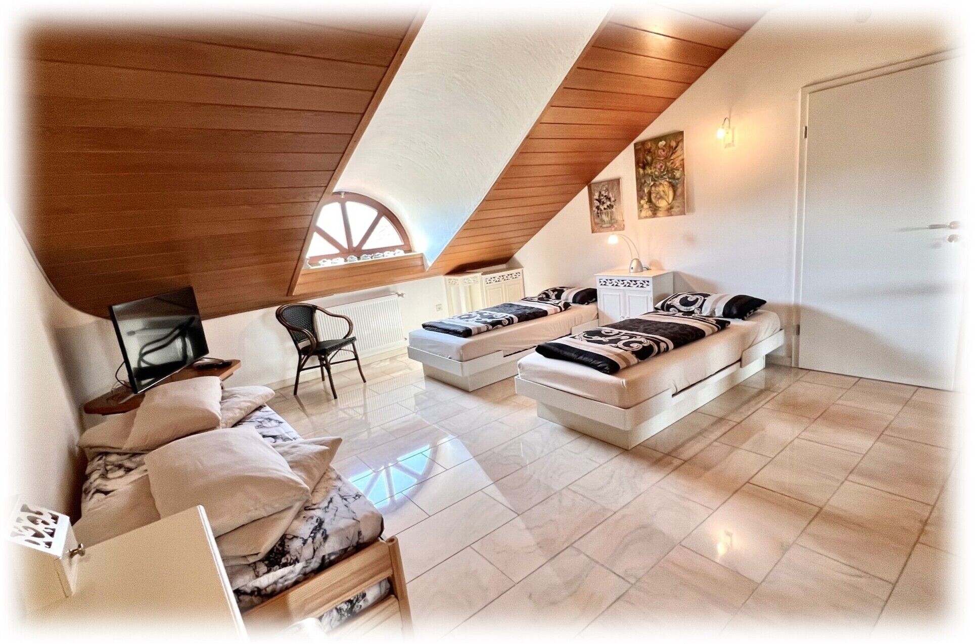 Ein Schlafzimmer im Loft-Stil mit schrägverdeckter Decke, zwei Betten, einem Sofa, einem Sessel und einem Fernseher.
