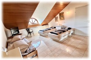 Camera in stile loft con soffitto spiovente, due letti, una divano, una poltrona e un televisore.
