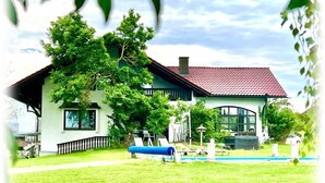 Una casa con techo rojo, un árbol grande en el frente y una piscina.