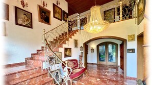 Una gran escalera con candelabro, escalones de mármol y obras enmarcadas en las paredes.