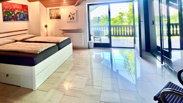 Un dormitorio con cama, radiador, escritorio y un amplio ventanal corredera que da a un balcón.