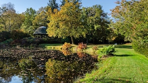 Uno stagno con ninfee, un gazebo e alberi con foglie autunnali.