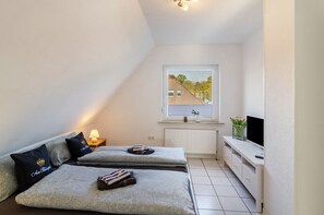 A small, well-lit room with two beds, a TV, and a window with a view of a building.