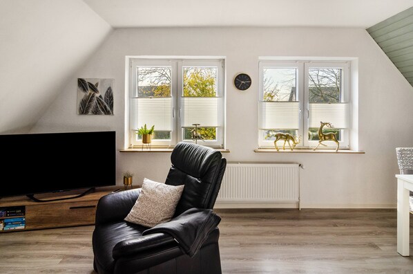 A modern living room with a leather sofa, a flat-screen TV, and a large window with blinds.