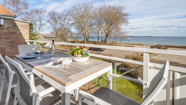 A wooden deck with a table and chairs, overlooking a body of water and trees.