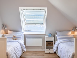 A bedroom with two beds, a window, a radiator, bedside lamps, and a small shelf with a toy.