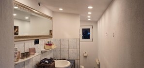 A compact bathroom with a marble vanity, a large mirror, and a small window.