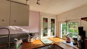 A kitchen with a wooden countertop, a kettle, a coffee maker, and a view of greenery outside.