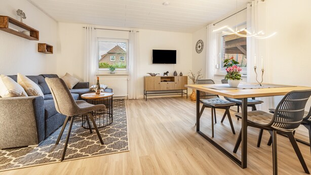 A modern living room with a sofa, chairs, a dining table, and a TV on the wall. - Apartment 'Celle-Bostel' with Private Terrace, Garden, and Wi-Fi (Celle)