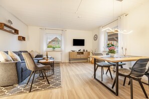 Un salon moderne avec un canapé, des fauteuils, une table à manger et un téléviseur fixé au mur.