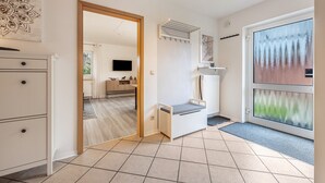 A modern interior with a white cabinet, a bench, a large window with a view, and a door leading to another room. - Apartment 'Celle-Bostel' with Private Terrace, Garden, and Wi-Fi (Celle)