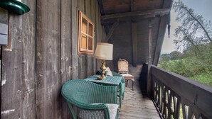 A wooden porch with a table and chairs, a lamp, and a window.