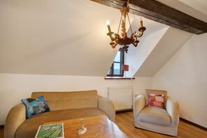 Un espacio tipo loft con techo de madera, una araña, un sofá, una silla y una mesa con un libro.