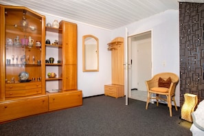 Een kamer met een houten kast, een rieten stoel, een spiegel en een behang met patroon.
