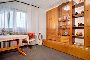 Een kamer met een houten kast, een tafel met een kantkleed, een stoel en een radiator.
