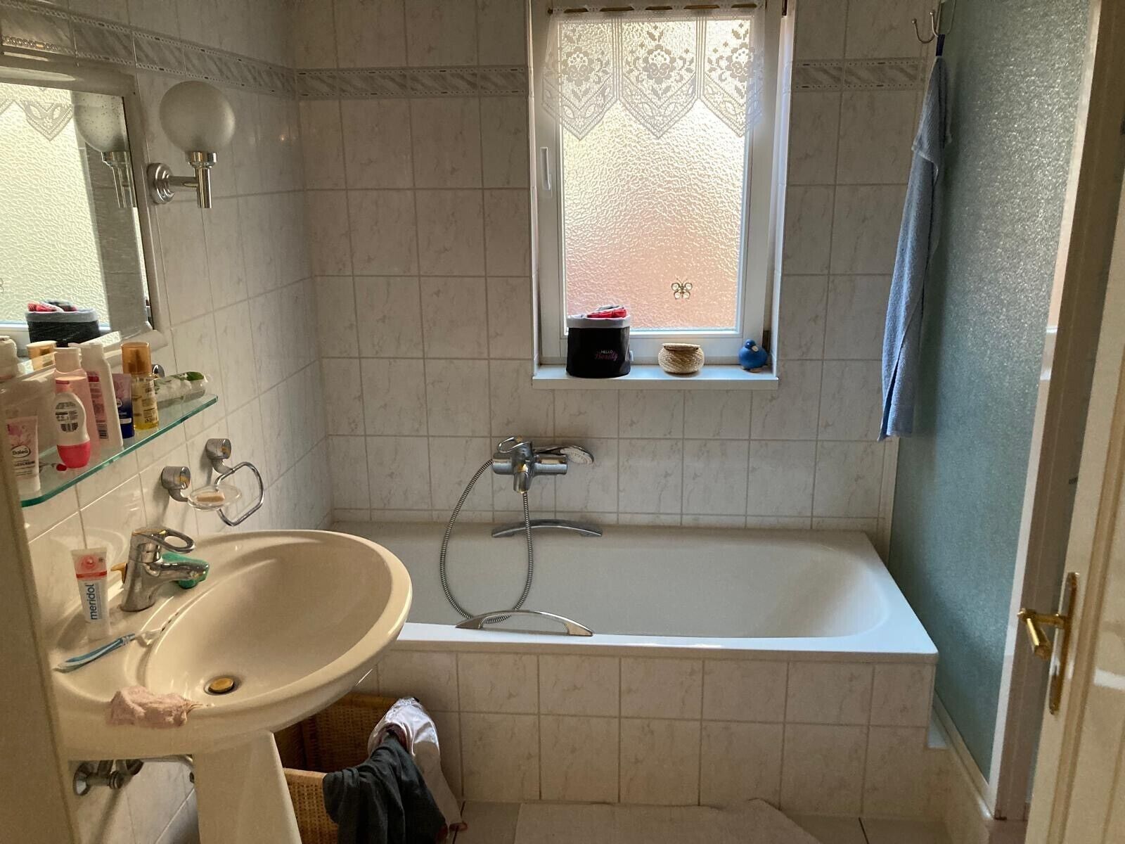 Un baño con bañera, lavamanos, ventana con vistas y estante con artículos de aseo.