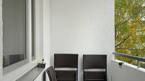 A balcony with two wicker chairs, a table, and a window. - Apartment 'Neuburg 7 - New' with Balcony and Wi-Fi (Neuburg an der Donau)