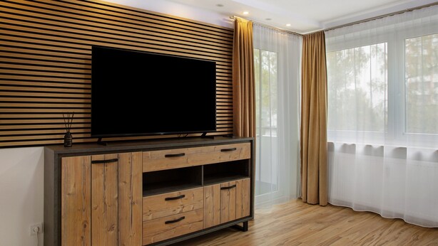 A modern living room with a wooden entertainment unit, a large flat-screen TV, and a large window with sheer curtains. - Apartment 'Neuburg 7 - New' with Balcony and Wi-Fi (Neuburg an der Donau)