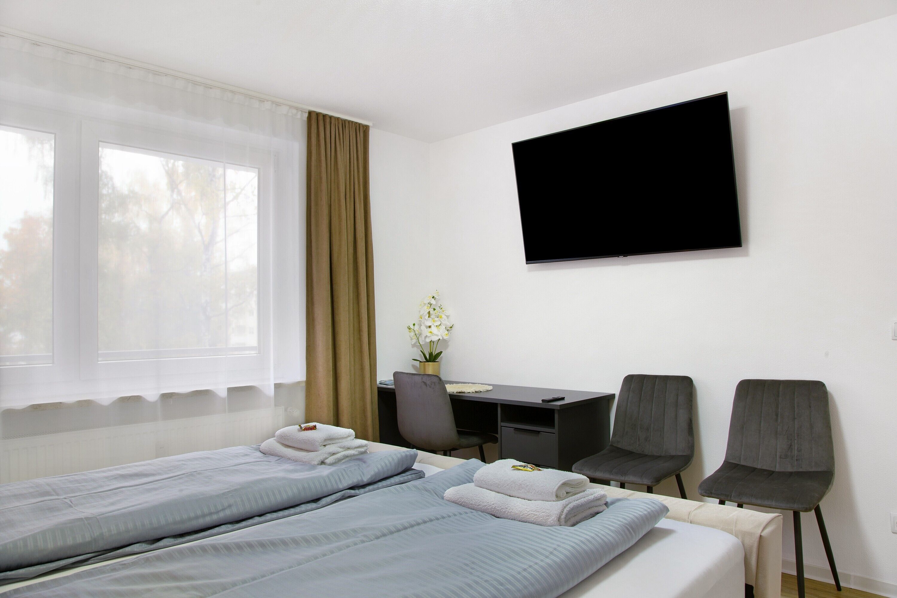 Une chambre d’hôtel avec deux lits, un bureau, deux chaises, une télévision et une fenêtre avec des rideaux.