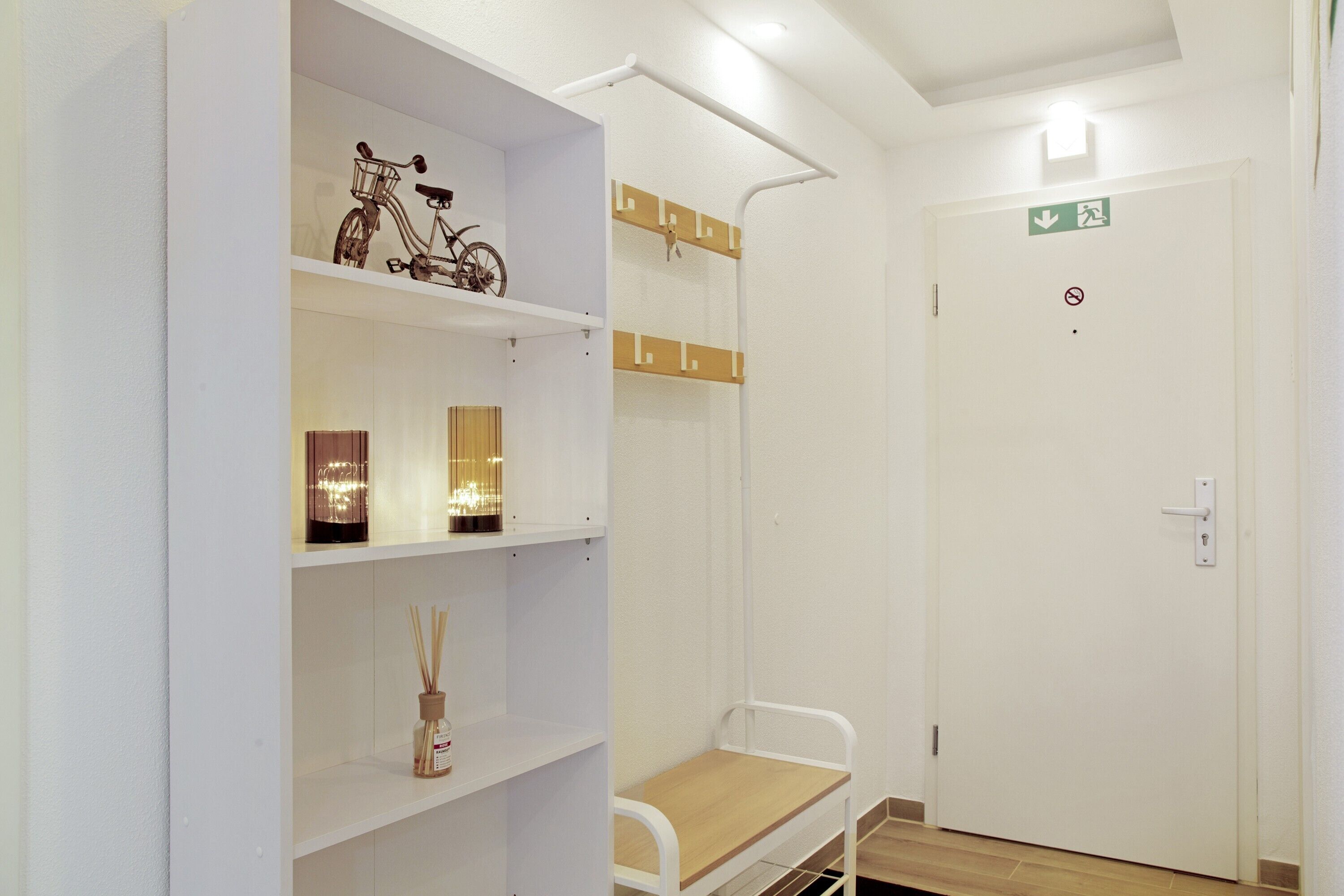 A room with a bunk bed, a shelf with a bicycle, a small table, and a door with an exit sign.