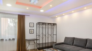 A modern living room with a grey sofa, a coffee table with magazines, a metal shelving unit with hangers, a small side table, and a window with sheer curtains. - Apartment 'Neuburg 7 - New' with Balcony and Wi-Fi (Neuburg an der Donau)