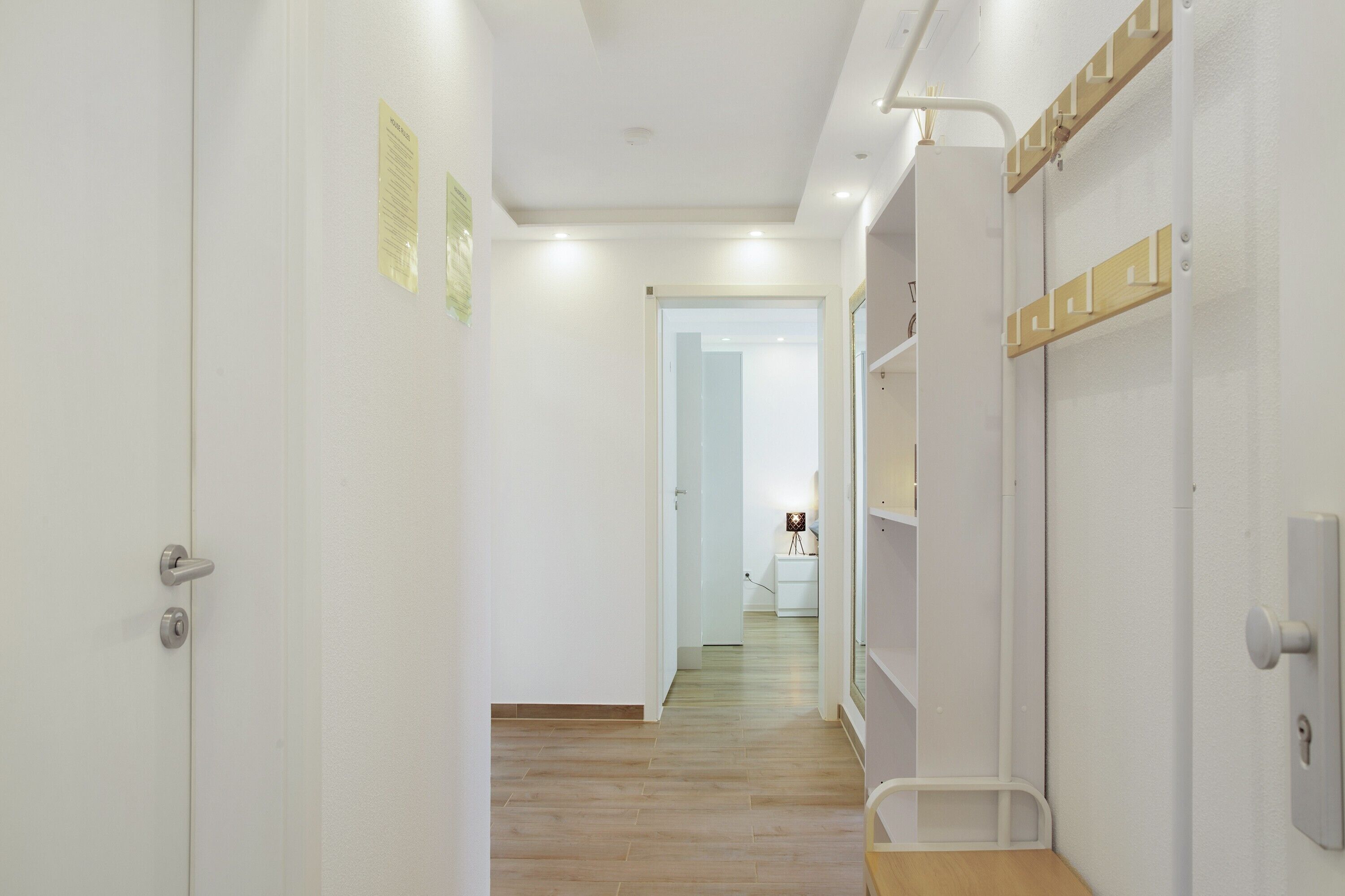 Un couloir doté d’un plancher en bois, de murs blancs et d’une porte avec une poignée en métal.