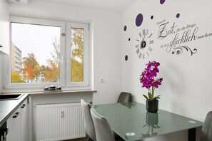 A modern kitchen with a window, a dining table with chairs, and a decorative wall clock.