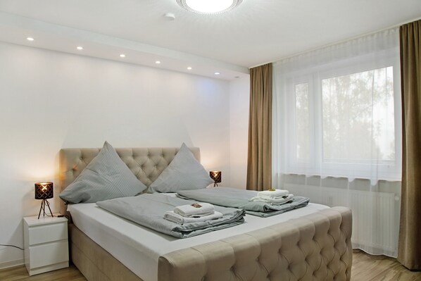 A neatly made bed with pillows, a bedside lamp, and a window with curtains.
