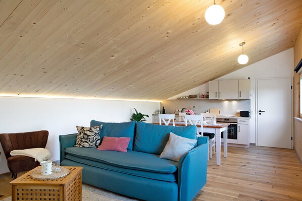 Een moderne woonkamer met een smaragdgroene bank, houten plafond en een keuken op de achtergrond.