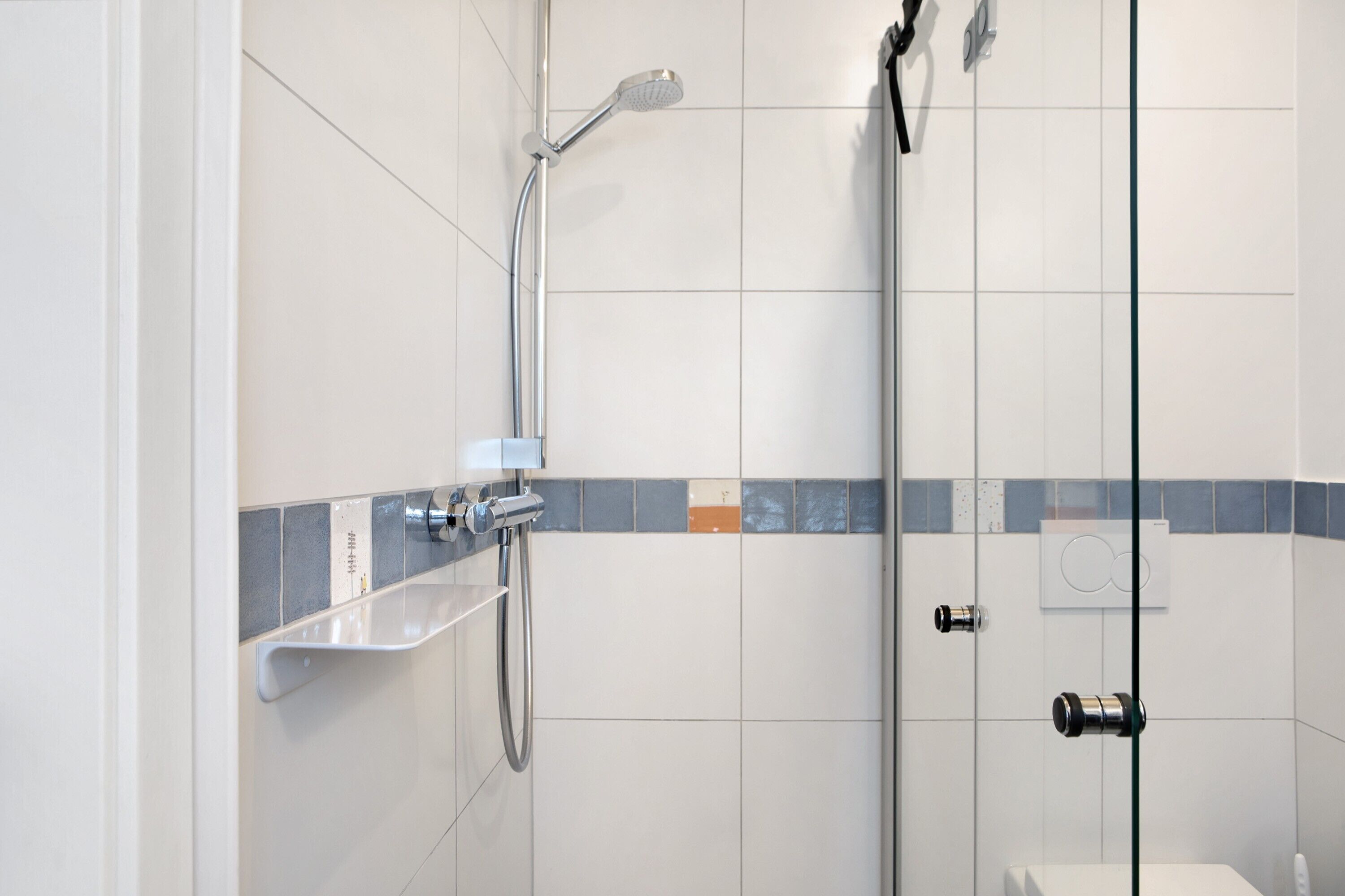 A modern bathroom with a glass shower enclosure, a white sink, and a tiled floor.