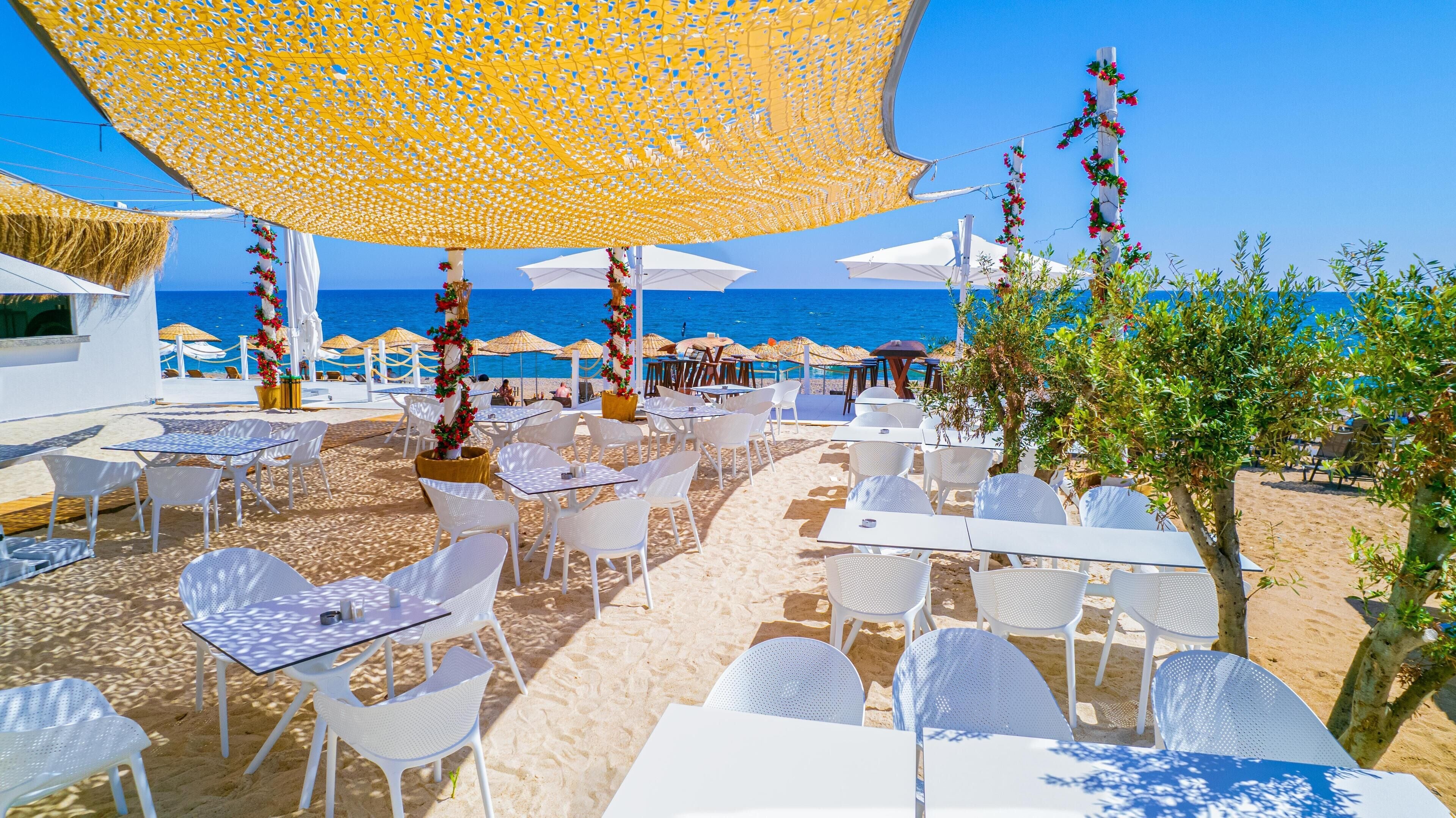 An outdoor seating area with white tables and chairs, umbrellas, and a view of the sea.