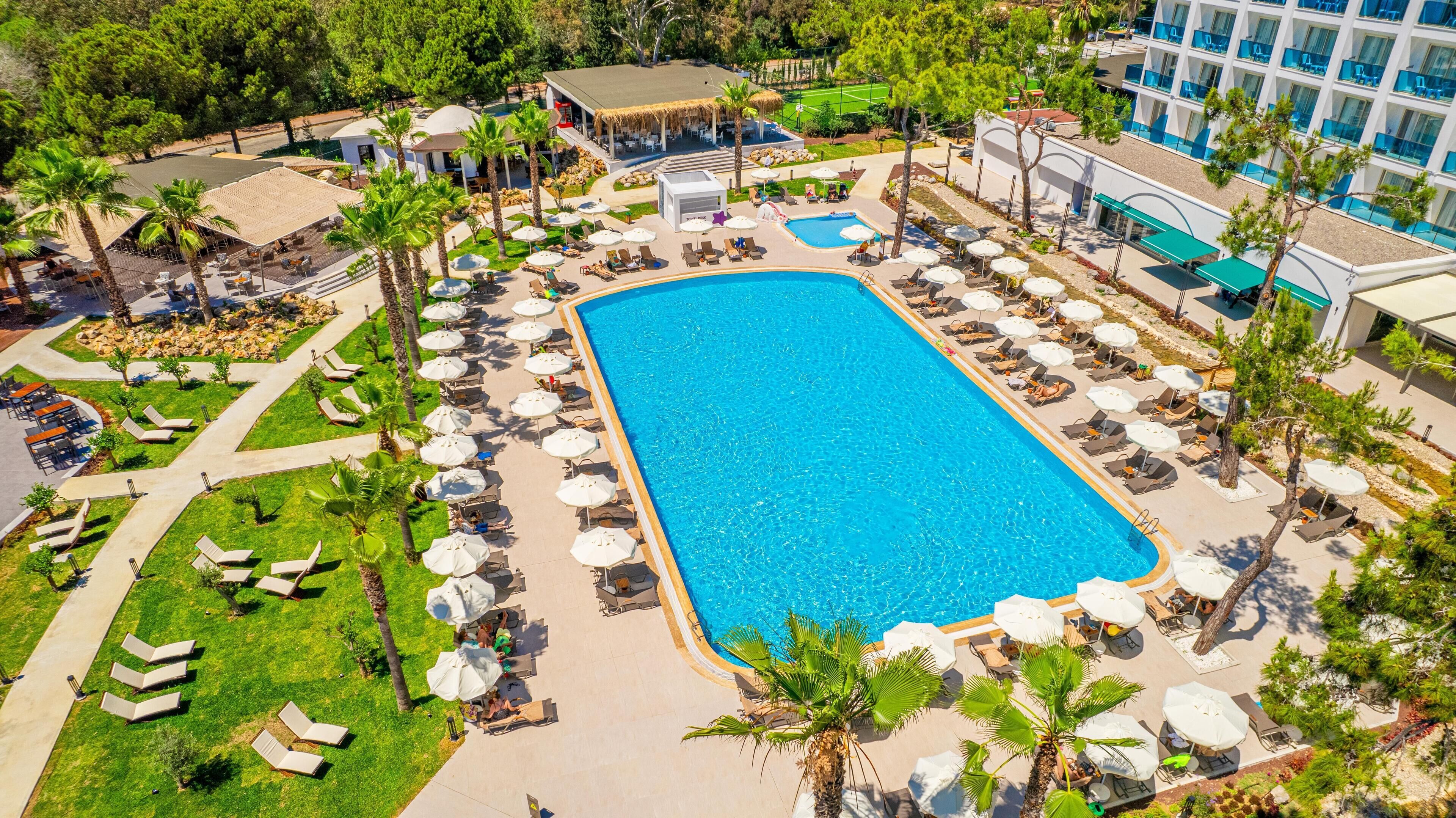A large rectangular pool surrounded by sun loungers and umbrellas, with a building in the background.