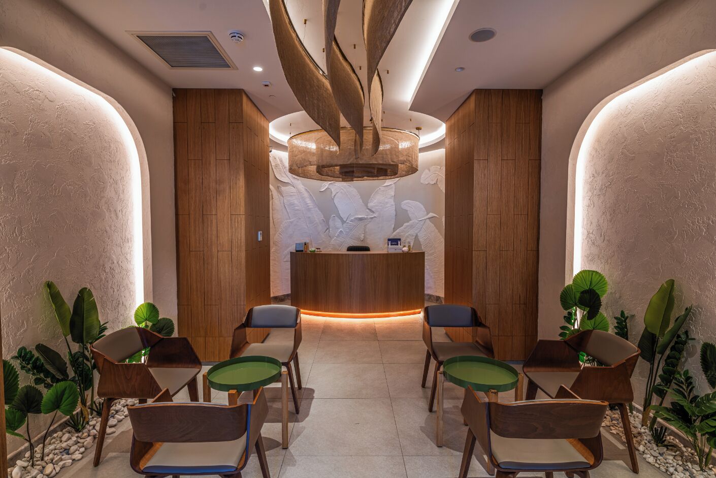 Un área de recepción con un mostrador de madera, una araña de cristal y varias sillas con cojines verdes.