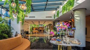 A modern lobby with a curved sofa, a marble floor, hanging plants, and a table with glassware and flowers. - Berry Blue Hotels - All Inclusive (Manavgat)