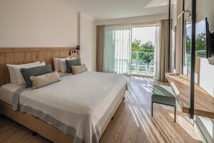 Habitación de hotel con una cama grande, cabecera de madera y un balcón con vistas a zonas verdes.